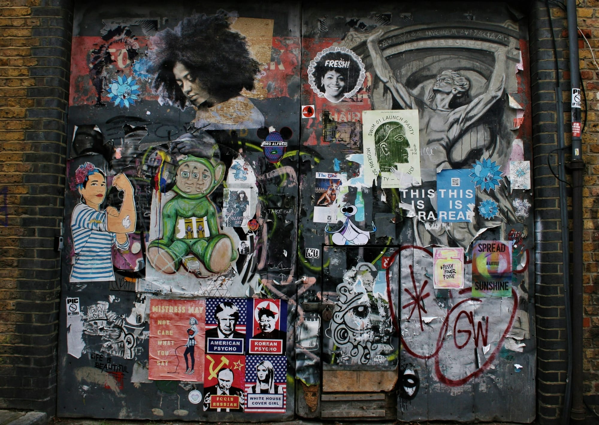 An urban wall covered with graffiti, torn posters, and colorful collages.